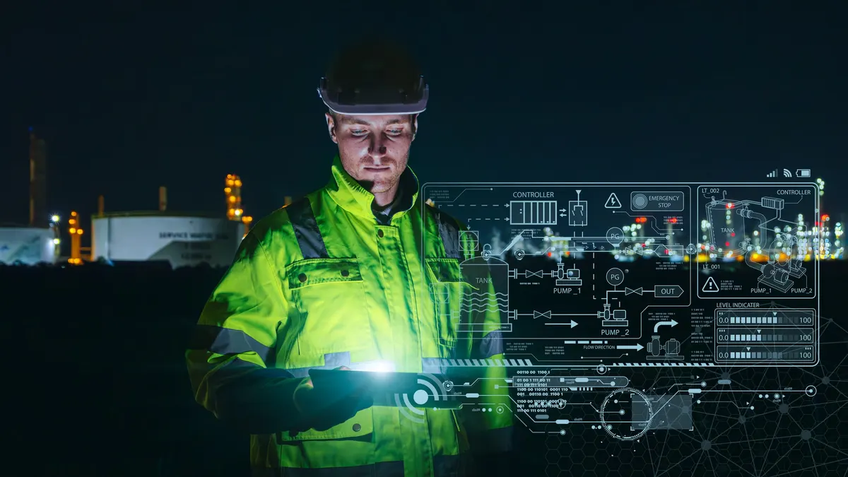A worker in a hi-vis jacket and hard hat at an industrial plant at night, looking down at a tablet, with a schematic of pumps, tanks and controllers overlaid beside him