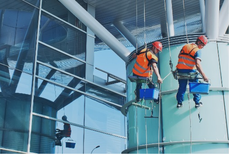 Two abseiling window cleaners in orange high-visibility vests and red helmets working down the curved glass facade of a modern building, with a third worker visible lower down