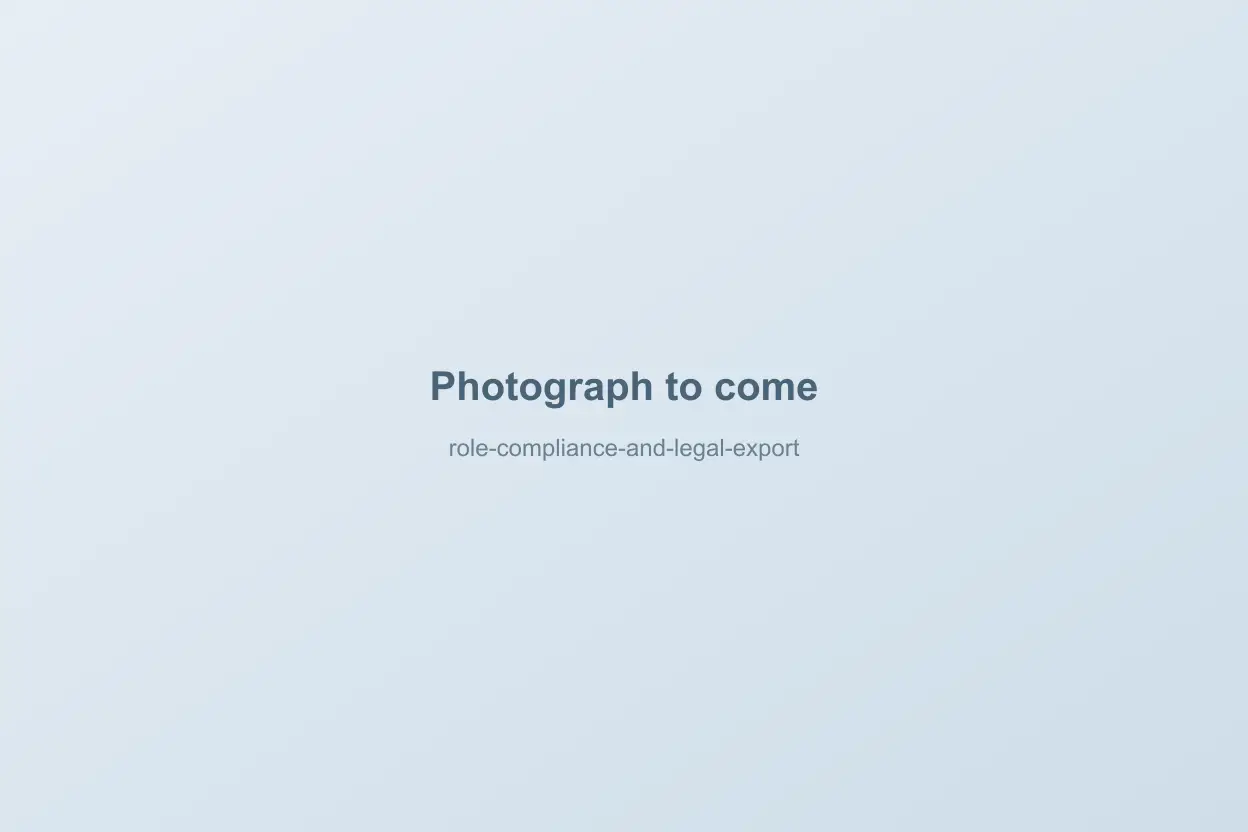 A compliance manager at a desk exporting a filtered contractor compliance record on a laptop, a printed regulator notice beside the keyboard, a meeting room visible through glass behind them
